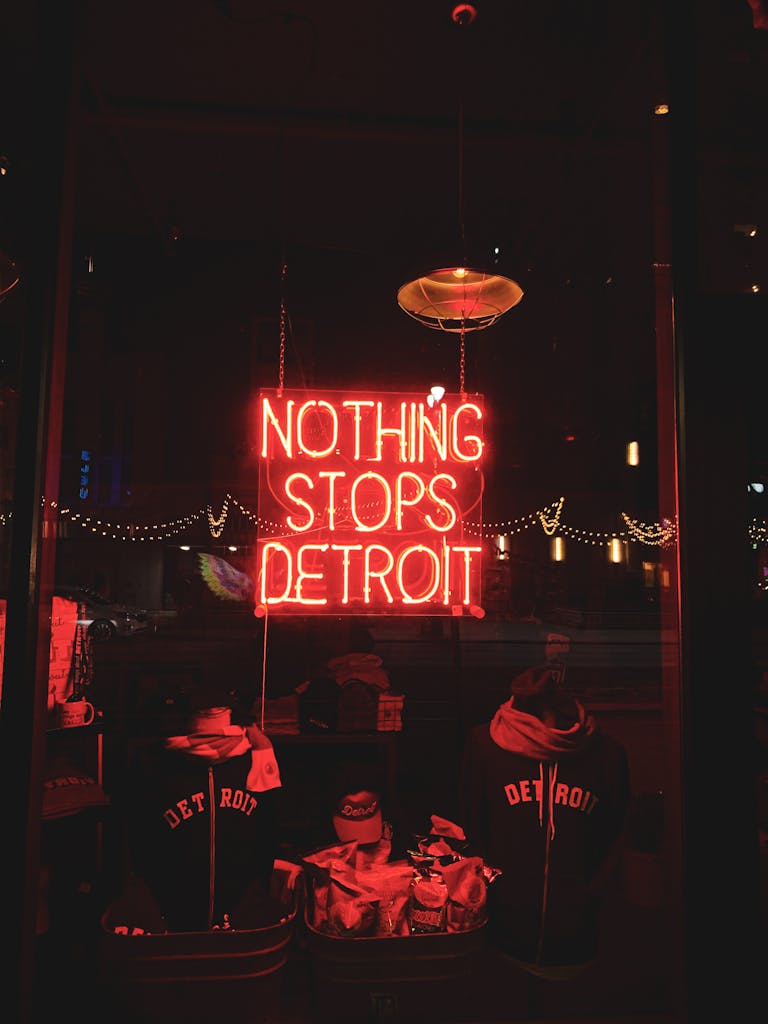 Vibrant neon sign reading 'Nothing Stops Detroit' adorns a storefront window, illuminating the city nightscape.