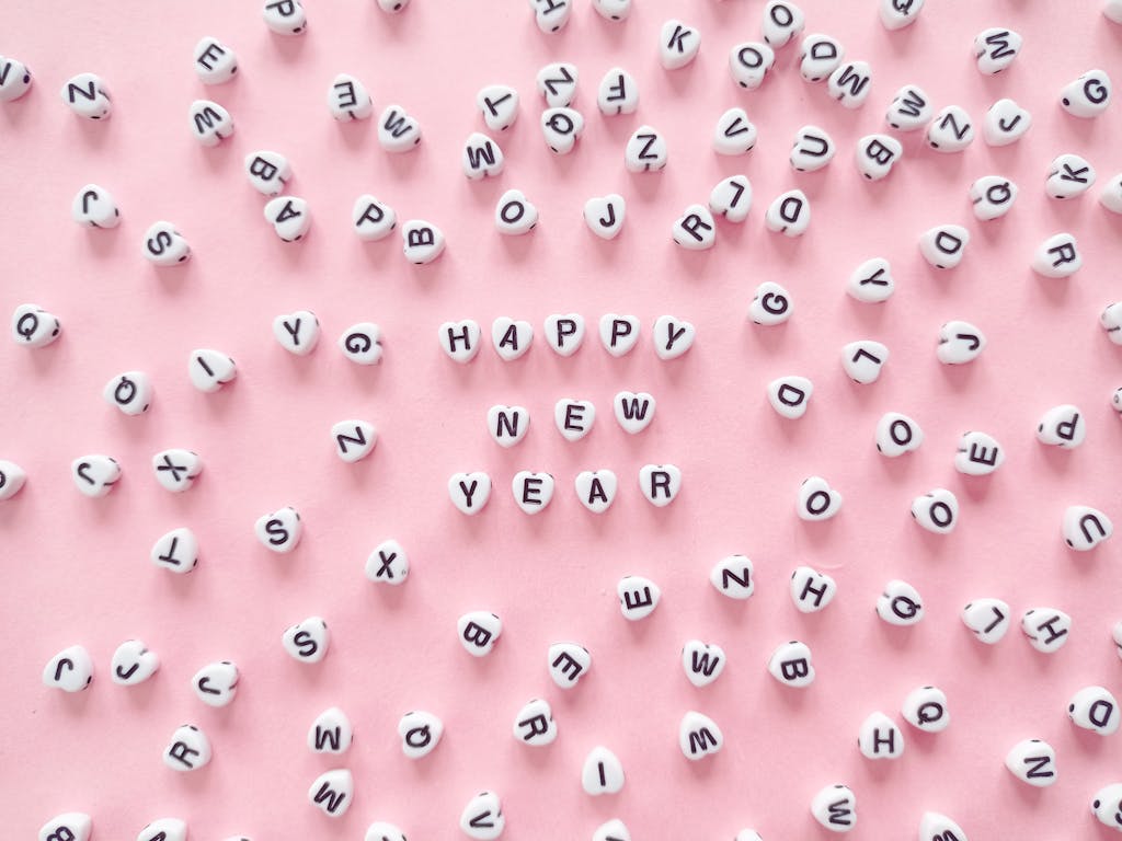 White beads forming 'Happy New Year' on a pink surface, symbolizing joy and celebration.